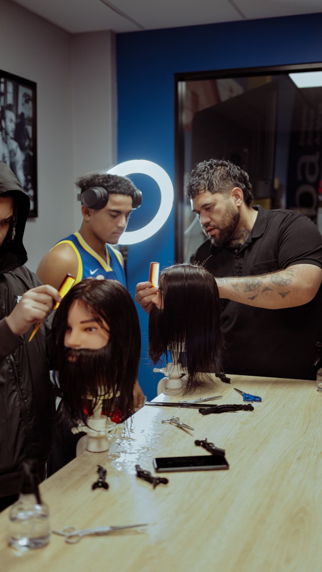 Rangatahi learning barbering alongside their tutor under the studio ring light