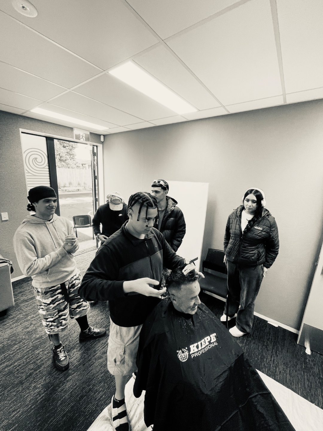 A rangatahi giving a real haircut while others look on in the Tūranga Aiga classroom